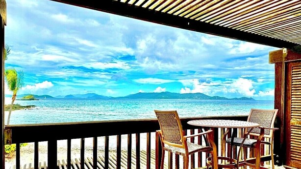 Un balcon avec deux fauteuils en osier et une petite table ronde, donnant sur une plage et la mer.