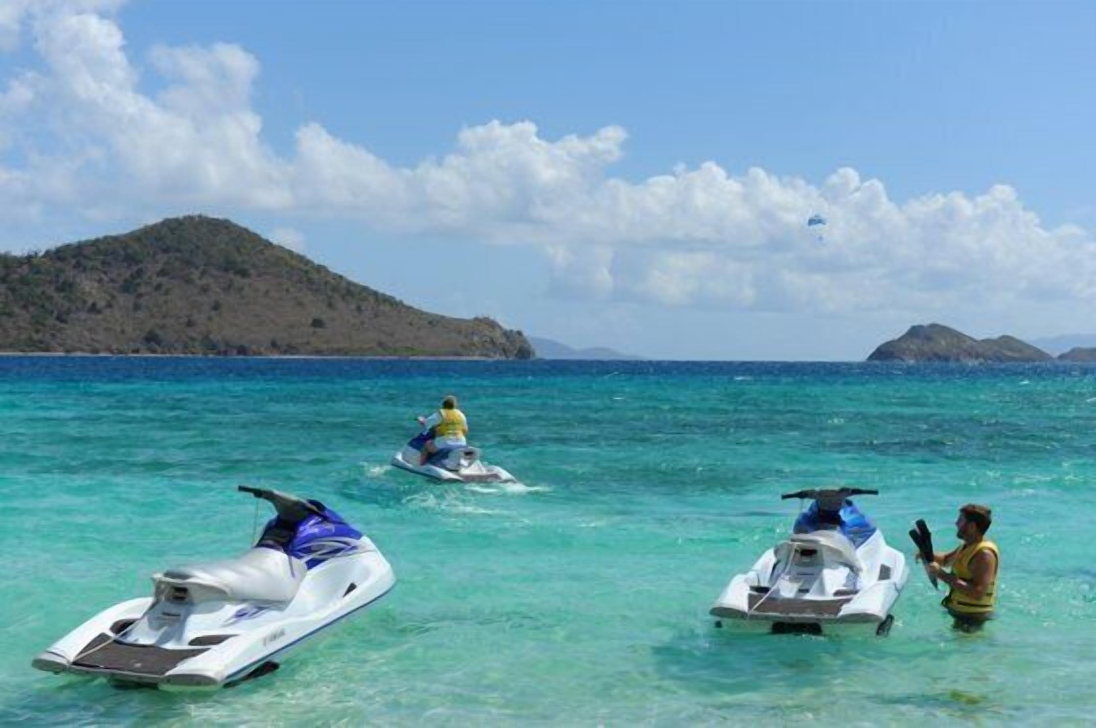 Mar azul y transparente con dos motos acuáticas y una persona en el agua.
