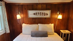 Een slaapkamer met een groot bed, twee bedlampen, een raamdecoratie met veerverbeelding en een klein nachtkastje met een zakdoos.