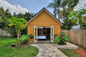 A small, single-story building with an open door leading to a bedroom with a bed and a desk.