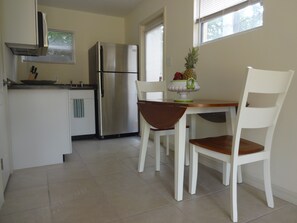 Une cuisine moderne avec des meubles blancs, un réfrigérateur en acier inoxydable et un coin repas comprenant une table en bois et des chaises blanches.