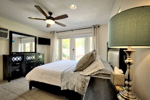 Une chambre à coucher comprenant un lit, un ventilateur de plafond, une table de chevet avec une lampe, une commode et un grand miroir.