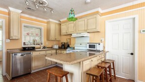 A kitchen with wooden cabinets, a stainless steel dishwasher, a white microwave, and a large island with stools.