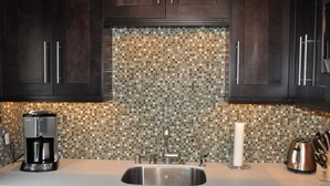 A kitchen with dark wooden cabinets, a Bosch dishwasher, a coffee maker, a kettle, and a tiled backsplash.