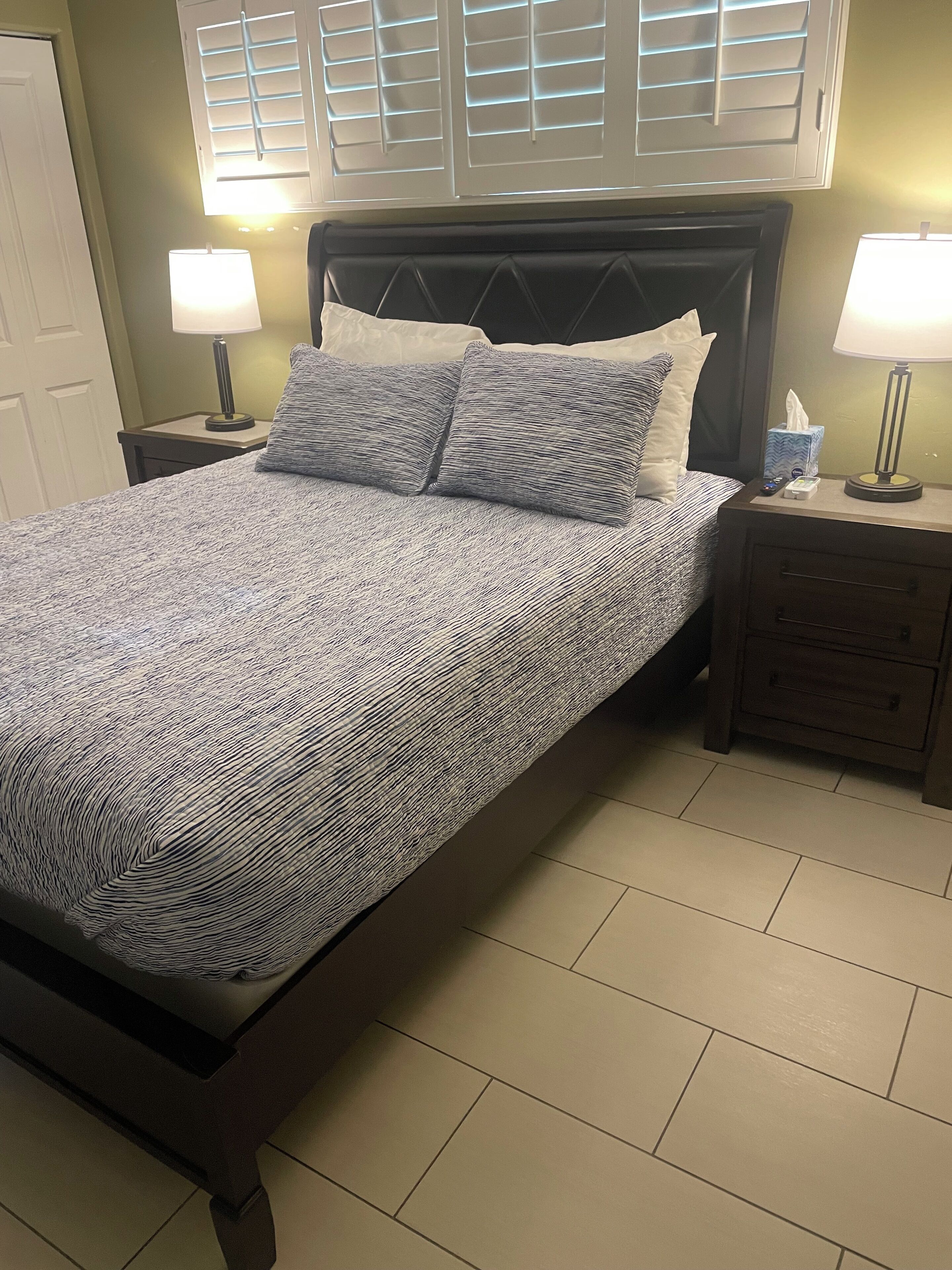A neatly made bed with a patterned bedspread and pillows, flanked by nightstands with lamps and a tissue box.