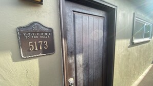 A dark wooden door with a keypad lock, a house number sign, and a small window above it.