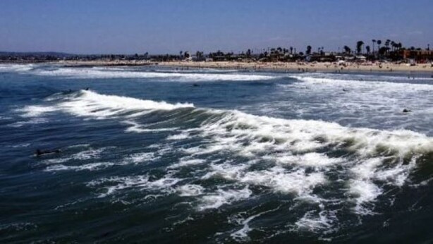 A beach with waves and a distant shoreline with buildings.