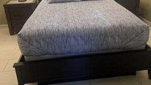 A bed with a patterned bedspread, two bedside lamps, a nightstand, and a window with blinds.