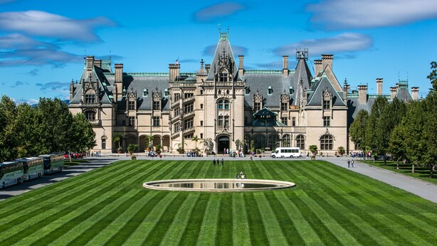 A large, historic building with a symmetrical facade, a central courtyard, and a well-maintained lawn.