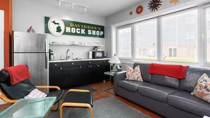 A modern living room with a sofa, a dining table, a kitchen area, and a sign reading 'Davidson's Rock Shop'.