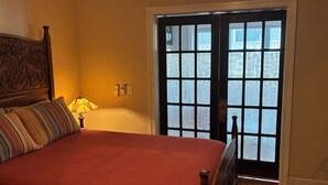 A bedroom with a bed, a lamp, a window with blinds, and a door.