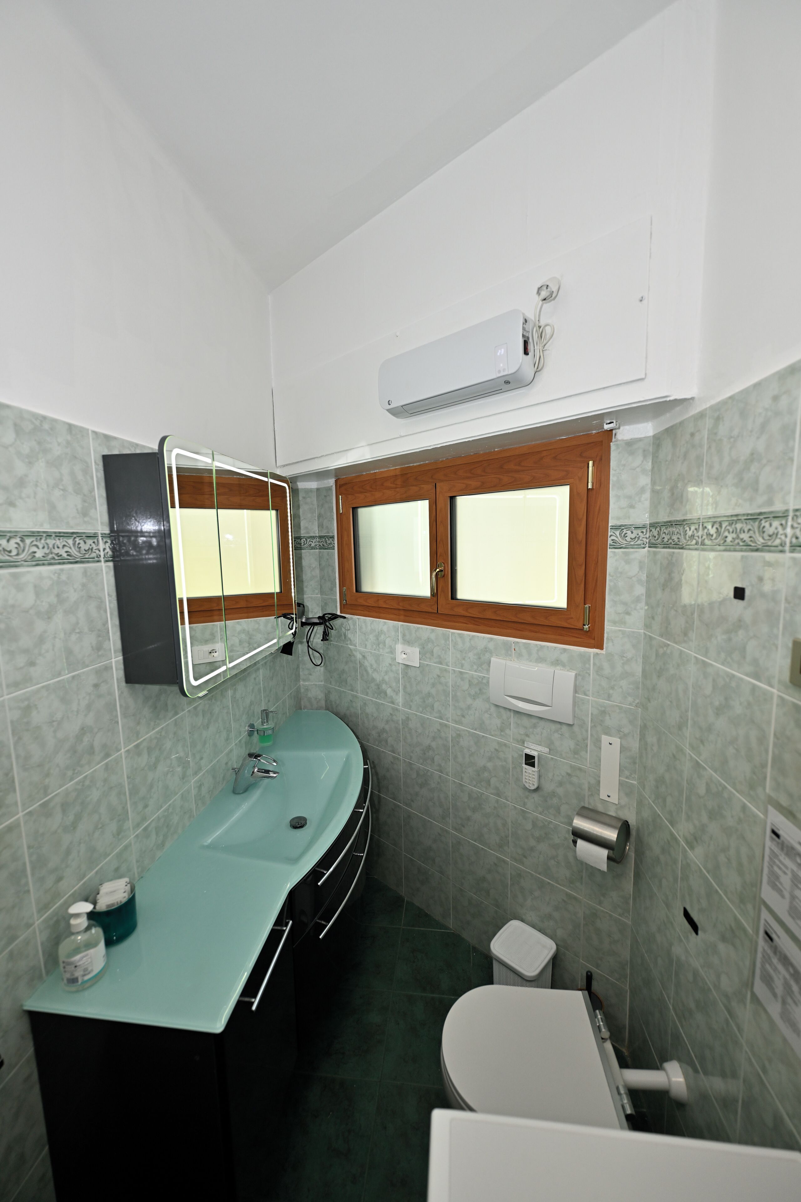 Ein Badezimmer mit Waschbecken, Spiegel, Toilette und Fenster.