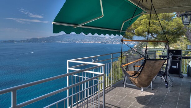 Een balkon met een hangstoel, een barbecue en uitzicht op zee.