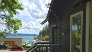 Ein Holzhaus mit Balkon und Seeblick, ein rotes Auto auf der Auffahrt, und ein klarer Himmel.