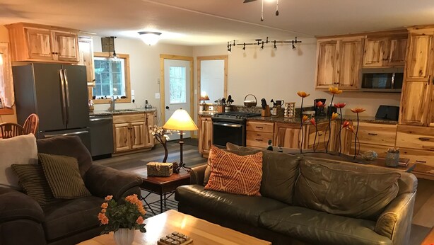 Ett rymligt vardagsrum med en stor soffa i läder, ett soffbord i trä och en köksdel med träskåp och moderna vitvaror.