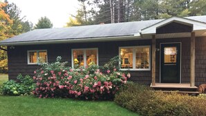 Ett hus med en mörk fasad, en välskött gräsmatta och en buske med rosa blommor framför.