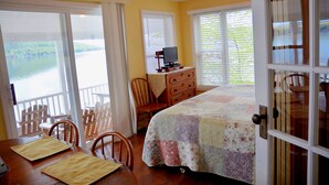 Un dormitorio con cama, cómoda, televisor y vista al lago a través de las ventanas.