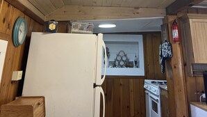 Interior de madera con una lámpara de techo, un refrigerador, un reloj y una estufa.