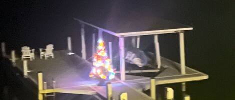 A dock with a Christmas tree and chairs.