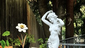 Un jardín con una estatua blanca, una flor y una cerca.