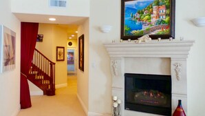 Una sala de estar con chimenea, una escalera y un cuadro de una escena costera.