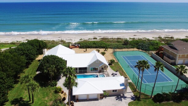 Una propiedad frente a la playa con piscina, cancha de tenis y vista al océano.