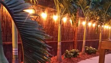 Un sentier bordé de palmiers et délimité par une clôture en bois, illuminé par des guirlandes lumineuses.