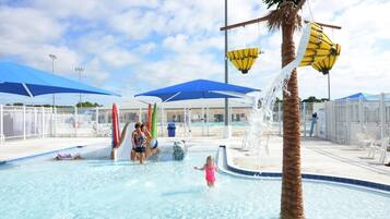 Un parc aquatique avec une piscine, des palmiers et des parasols bleus.