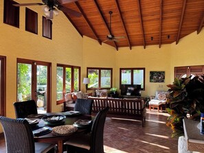 A spacious living area with a high ceiling, a television, and a dining table set for four. - Amazing Whitewater View Of The Ballena Marine Preserve Islands (Uvita)