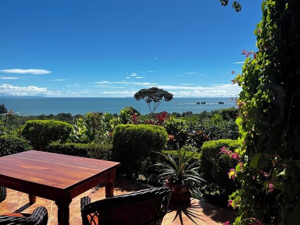 An outdoor patio with a wooden table and chairs, surrounded by lush greenery and a view of the sea. - Amazing Whitewater View Of The Ballena Marine Preserve Islands (Uvita)