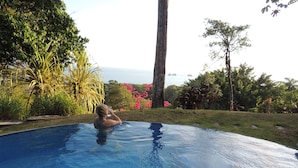 A person relaxing in a swimming pool with a view of the sea and lush greenery. - Amazing Whitewater View Of The Ballena Marine Preserve Islands (Uvita)