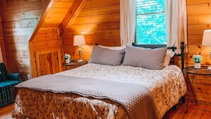 Een gezellig slaapkamer in een houten blokhut, met een bed, een plafondventilator en een raam met gordijnen.