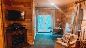 Een knus interieur van een chalet met een televisie, open haard, bank en een tafelvoetbaltafel.