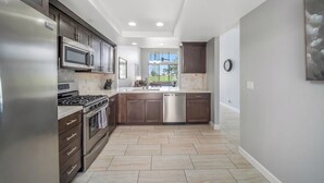 A modern kitchen with stainless steel appliances, dark wooden cabinets, a central island, and a large window providing a view of the outdoors. - Completely Renovated PGA West - Stadium Course -  Lic #259026 (La Quinta)