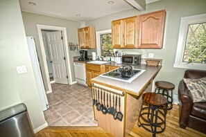 A compact kitchen with wooden cabinets, a microwave, and a coffee maker. There are stools and a window with a view of greenery.