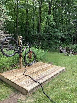 A wooden platform with a bicycle mounted on a stand, surrounded by a forested area.