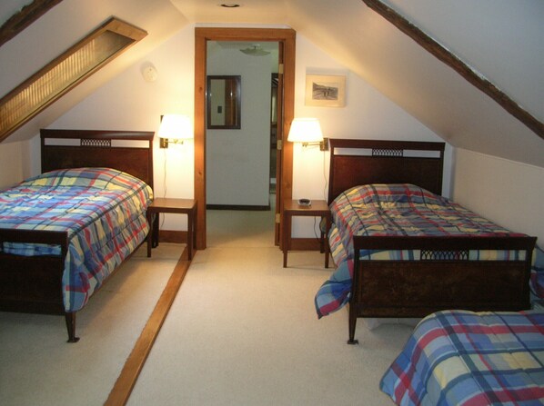 A bedroom with two single beds, a wooden headboard, a small bedside table with a lamp, and a door leading to another room. - NH Country Retreat Family Reunions & Weddings (Tamworth)