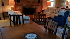 A cozy living room with a brick fireplace, a sofa, a dining table, and a TV.