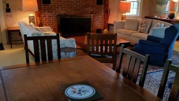A cozy living room with a brick fireplace, a sofa, a dining table, and a TV.