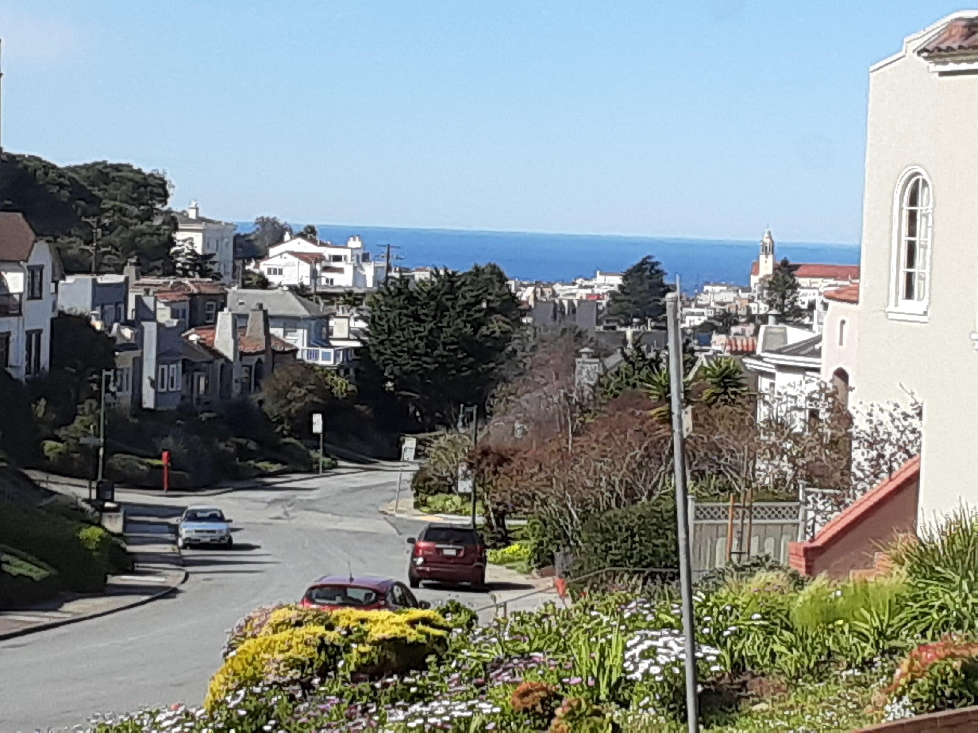 A residential street with houses, a church, and a view of the ocean.