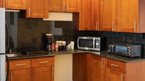 Una cocina con armarios de madera, encimera de granito, refrigerador, microondas y tostadora.