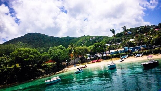A coastal scene with boats docked near a sandy beach, surrounded by lush greenery and hills.