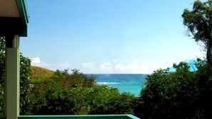 A balcony with two white rocking chairs facing a view of the ocean and lush greenery.