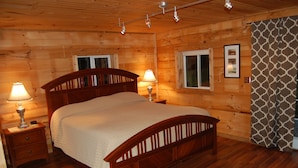 Ein Schlafzimmer einer Holzhütte mit einem großen Bett, zwei Nachttischen mit Lampen und einem Fenster mit Vorhängen.