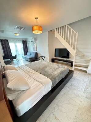 A modern bedroom with a large bed, a TV, a staircase, and a seating area with a sofa and chairs.