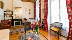 A living room with a fireplace, a dining area, and a large window with red curtains.