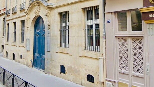 A historic building with a prominent blue door, multiple windows with metal bars, and a balcony with ornate railings.