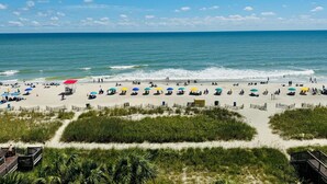 A beach with rows of umbrellas and beach chairs, a lifeguard tower, and a wooden boardwalk leading to the beach. - 💎NEWLY REMODELED!! ISLAND TIME Honeymoon Suite Direct Oceanfront King Luxury (Myrtle Beach)