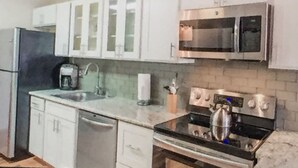 Una cucina con mobili bianchi, un forno a microonde, un fornello e una lavastoviglie.