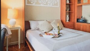 Un letto rifatto con cuscini e una bottiglia di vino, un tavolino con una lampada e mobili in legno con vetrate.